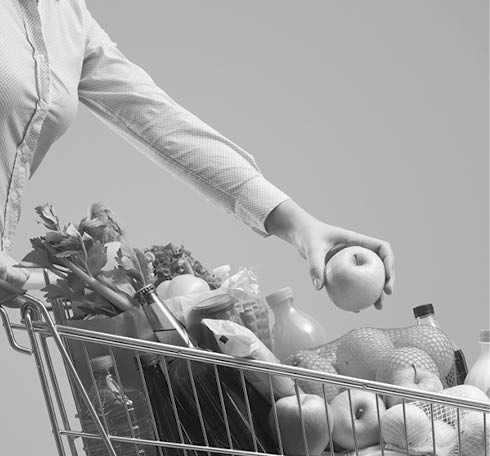 Young woman putting goods in her full shopping cart, grocery shopping banner with copy space