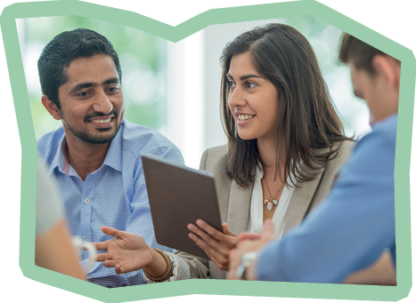 A multi-ethnic group of young business men and women in semi-casual office clothes are sharing ideas and holding a digital tablet in an indoor, sunlit office.